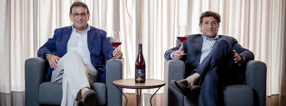 Two members of the Neri family seated with glasses and a bottle of Neri wine